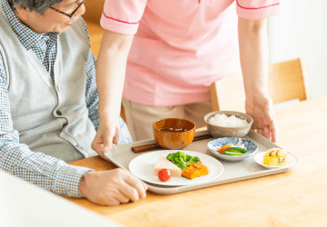 A caregiver serves a meal to an older man at home.