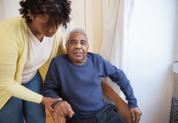 A caregiver offers a steady hand to an older man at home.