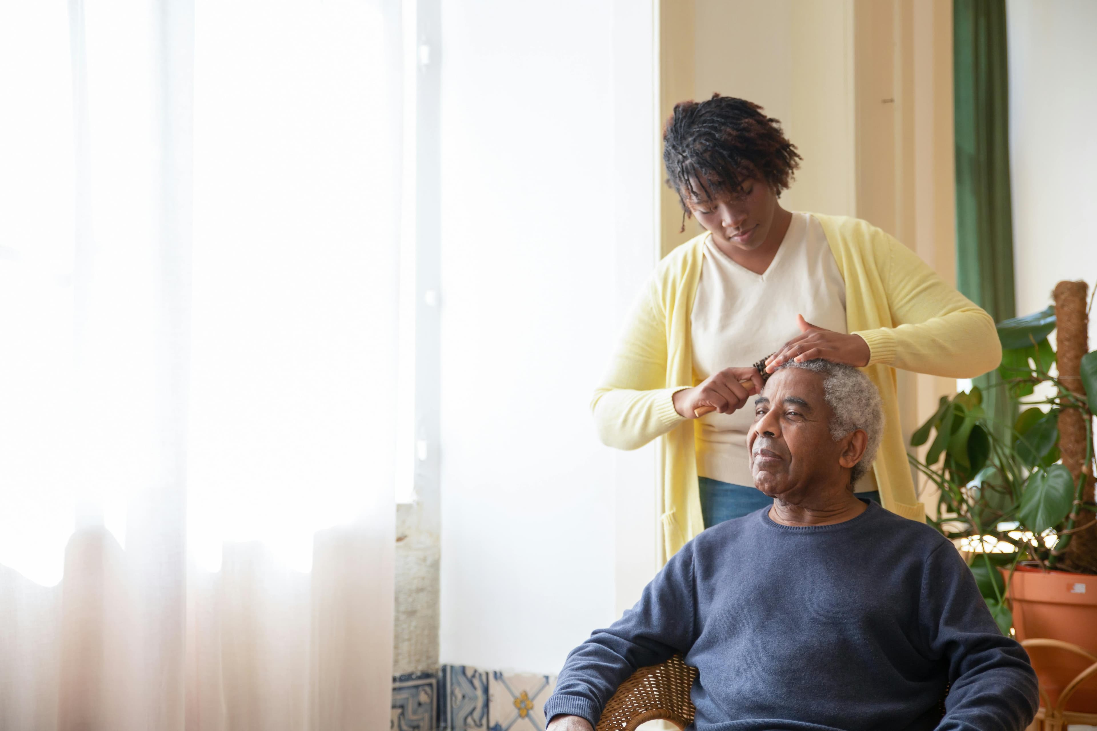 A caregiver helps an older man with his morning grooming routine.