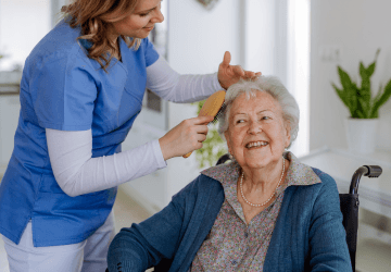 A caregiver gently brushes an older woman’s hair.